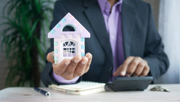 man holding model house at desk with calculator